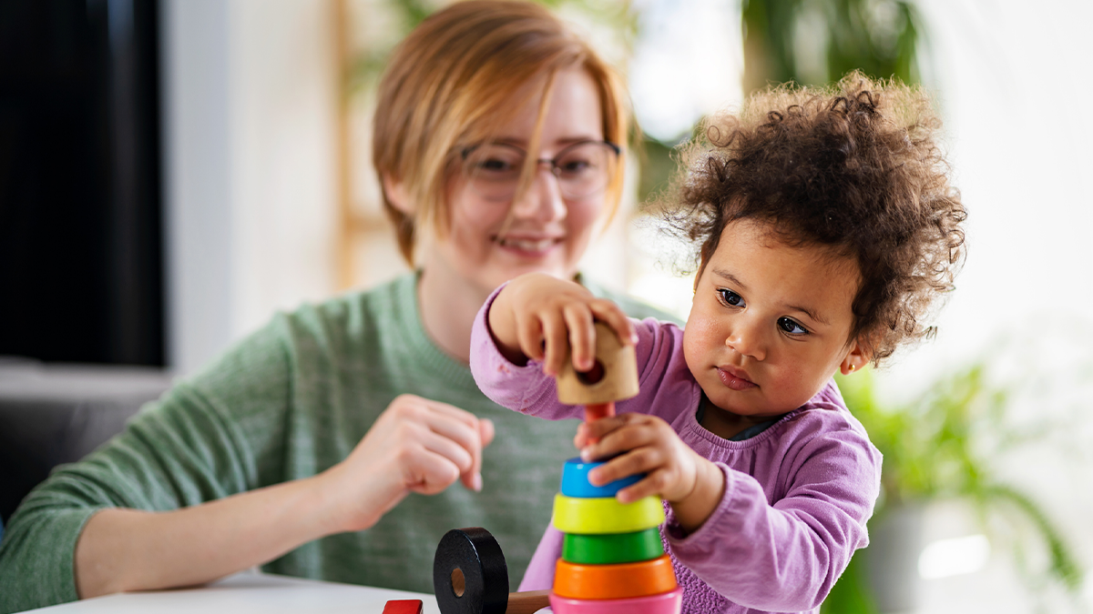 Teacher sitting with toddler, playing with building blocks