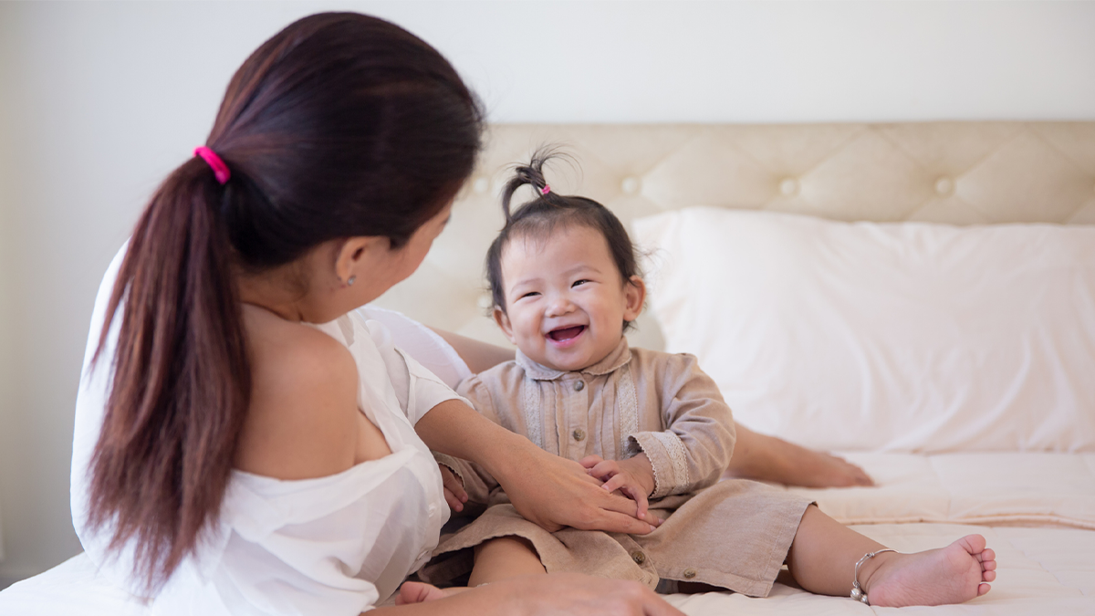 Mother holds smiling baby in her lap.