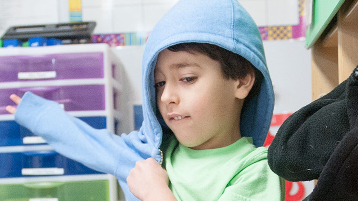 Niño de 3 años poniéndose la chaqueta.