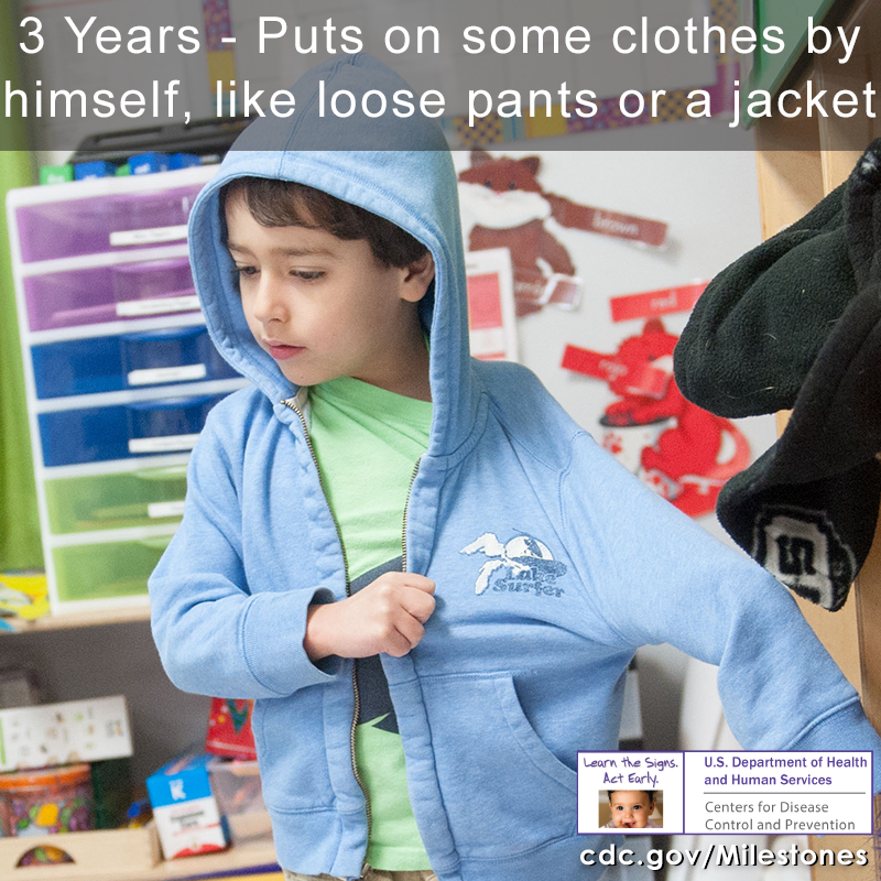 The boy in this photo is putting on a blue hoody by himself, a 3 year milestone.
