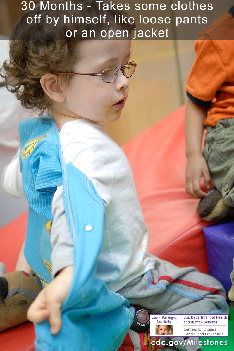 The boy in this photo is taking his blue jacket off by himself, which is a 30 month milestone.