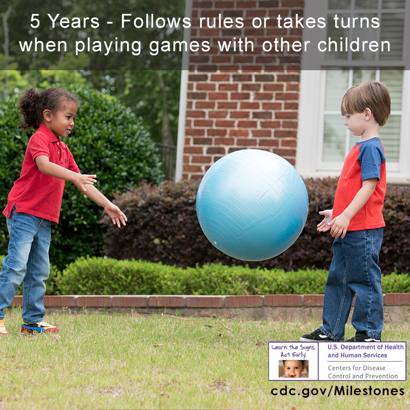 The children in this photo are throwing a blue ball back and forth, a 5 year milestone.