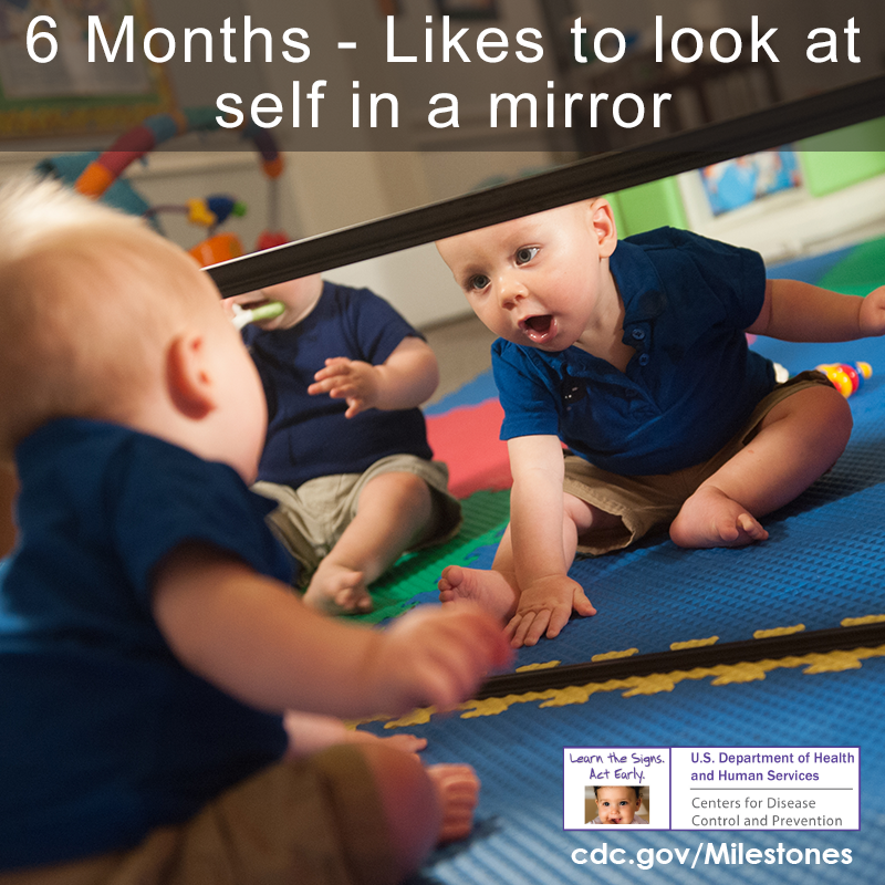 Baby looking at self in the mirror while sitting on the ground