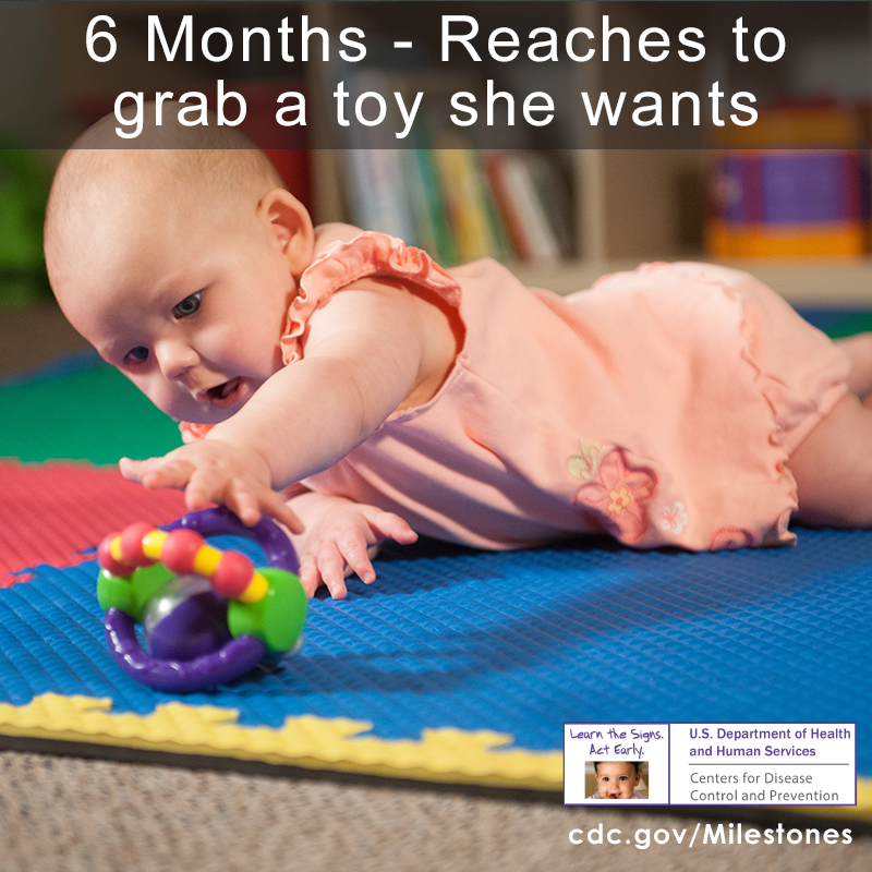 Baby laying on belly is reaching for a toy on the ground
