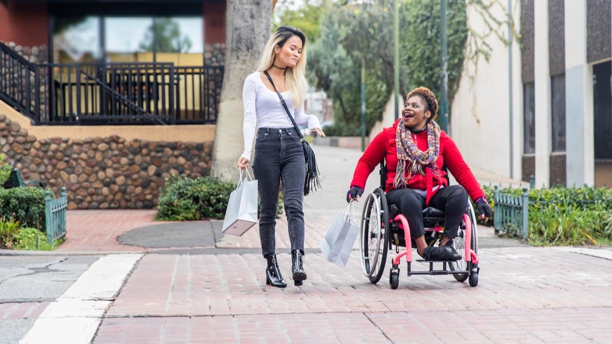 Two women, one in a wheelchair, crossing the street at a safe place to do so.