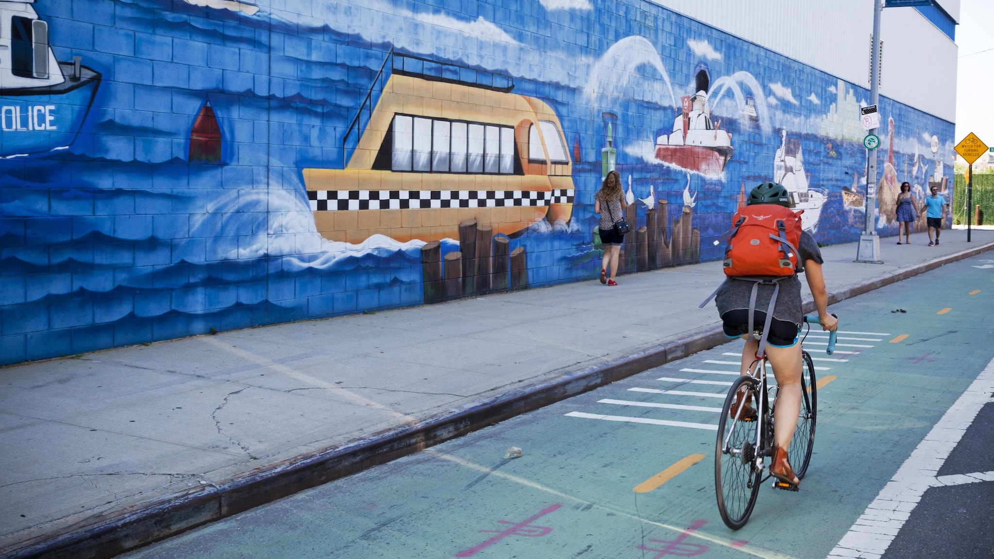 Woman biking on bike path next to mural.