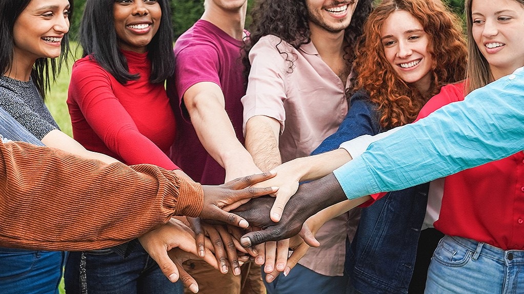 Diverse group of people putting their hands together in a circle.