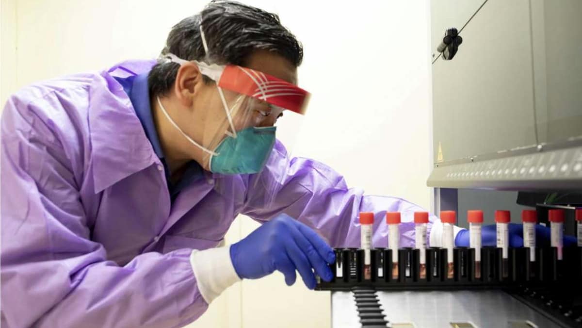 Man with laboratory safety gear slides vials into a machine.