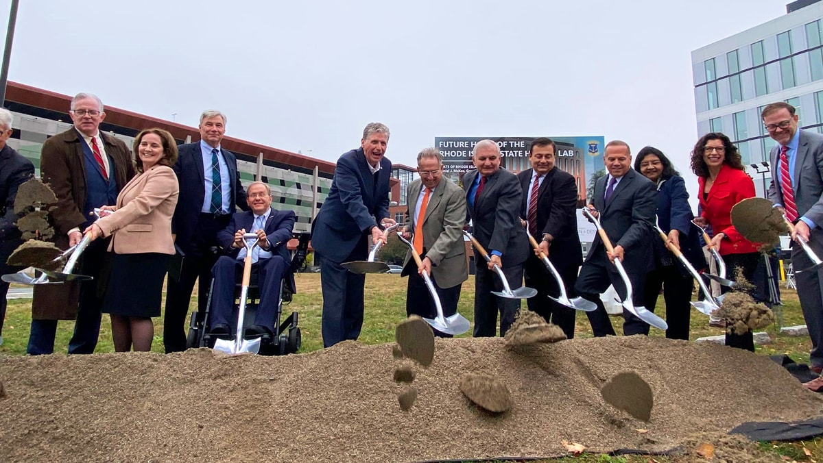 Thirteen people with shovels scooping and throwing out dirt toward the camera