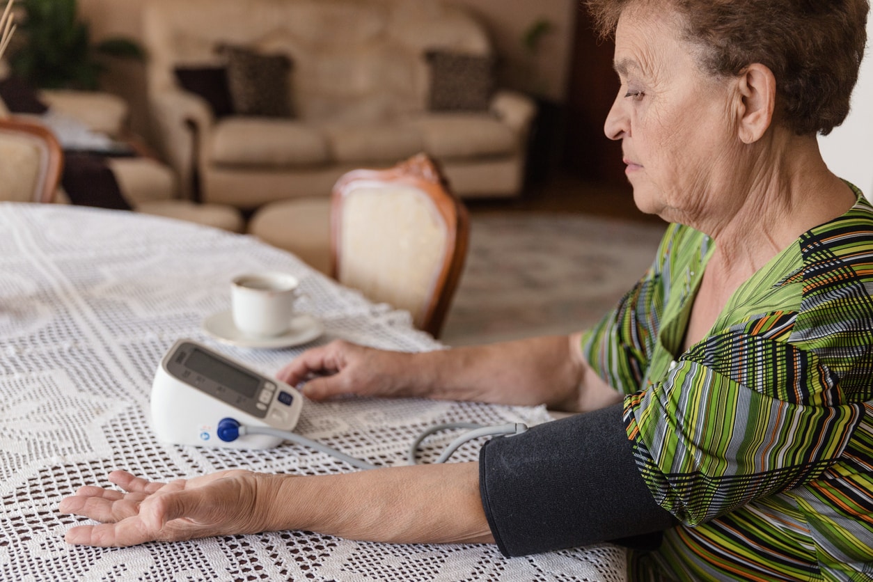Mujer mayor tomándose la presión arterial en la mesa del comedor