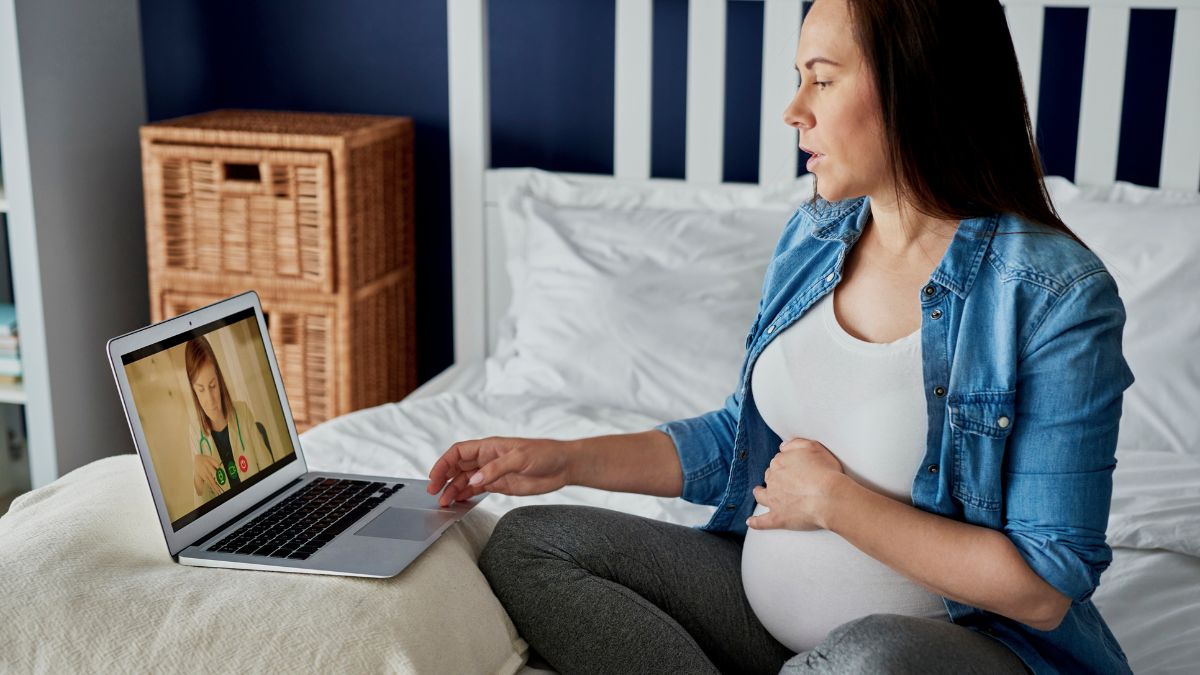 Pregnant woman sitting on bed looking at laptop screen