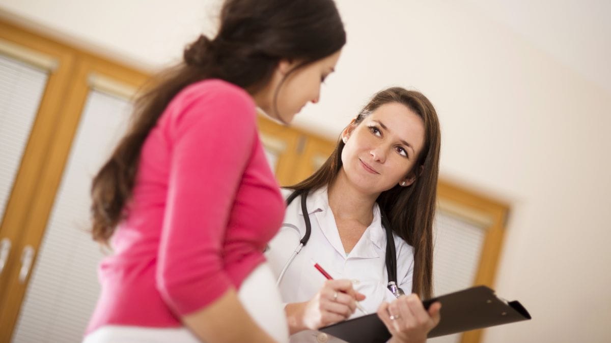 Healthcare professional asking a patient questions and writing on a clipboard