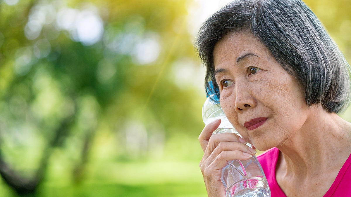 Asian woman holds plastic bottle of water to her face to cool.