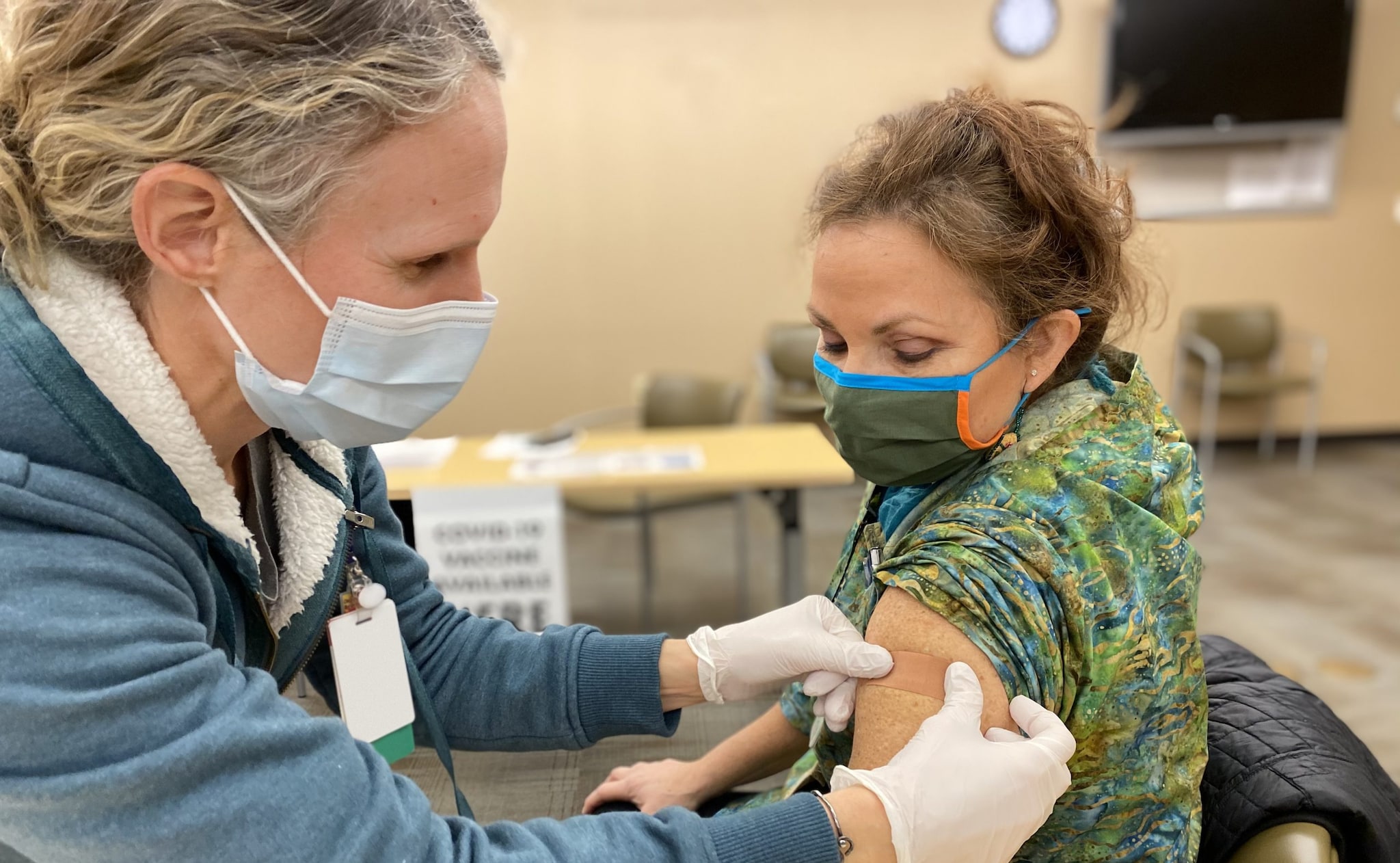 Healthcare professional places band aid on arm of recently vaccinated woman.