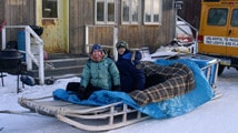 People on dogsled in front of building