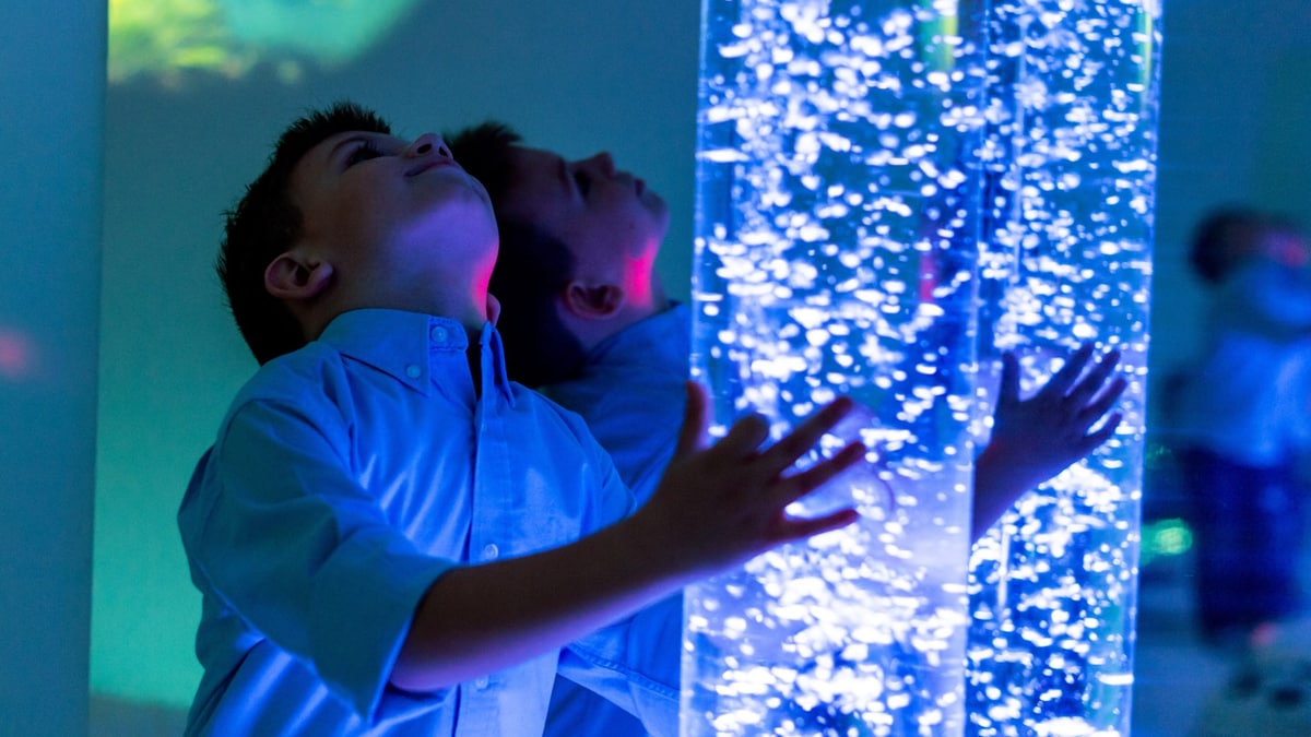 Child interacting with colored lights bubble tube lamp during therapy session.