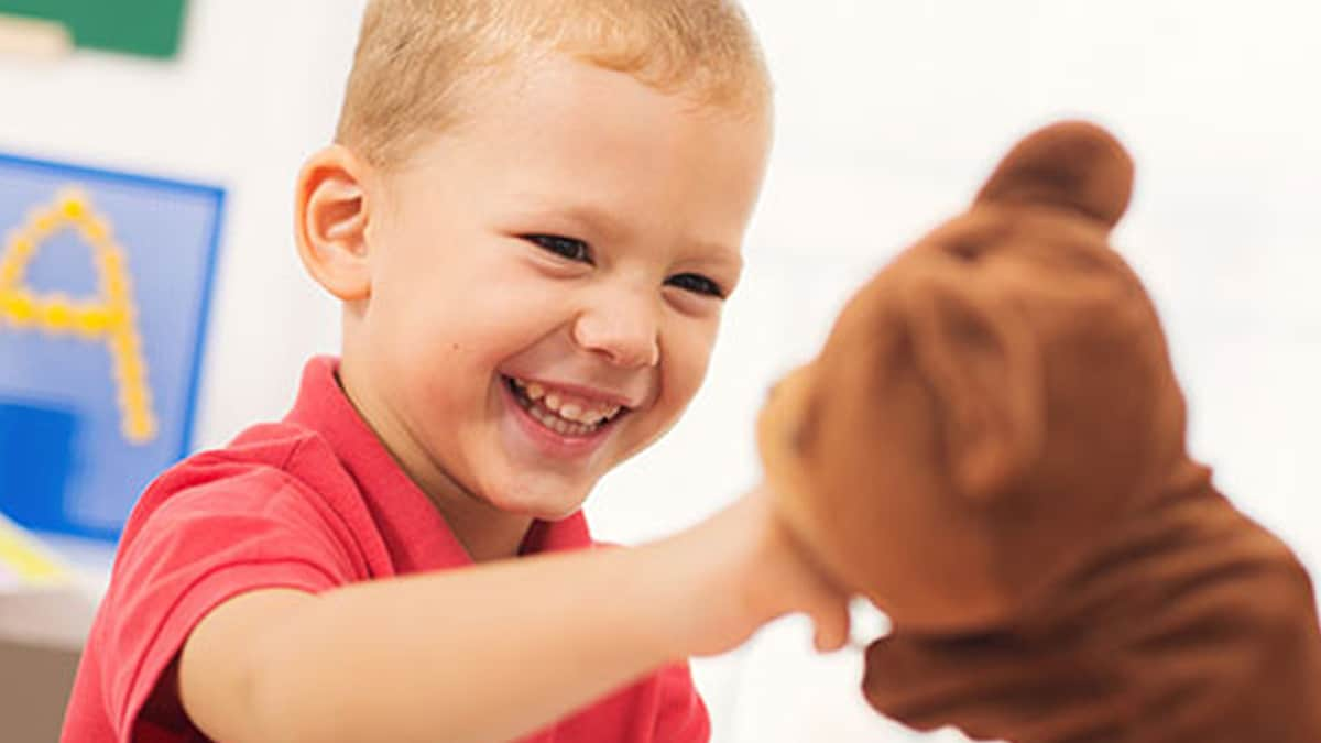 Niño sonriendo mientras juega con un oso de peluche en un salón de clases.