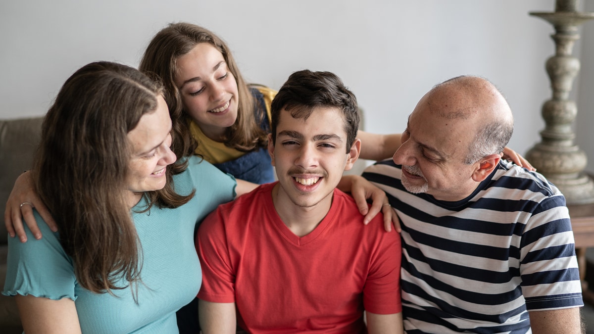 Family hugging and smiling with young adult son in the center