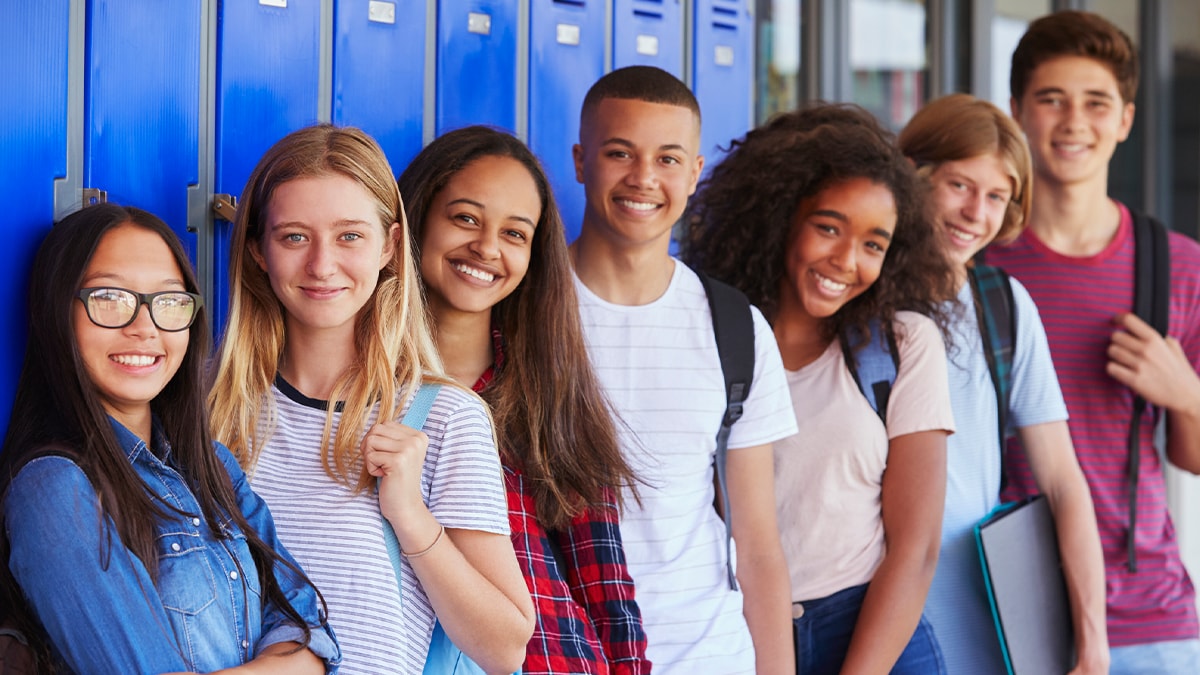 Group of high school students smiling, standing next to school lockers.