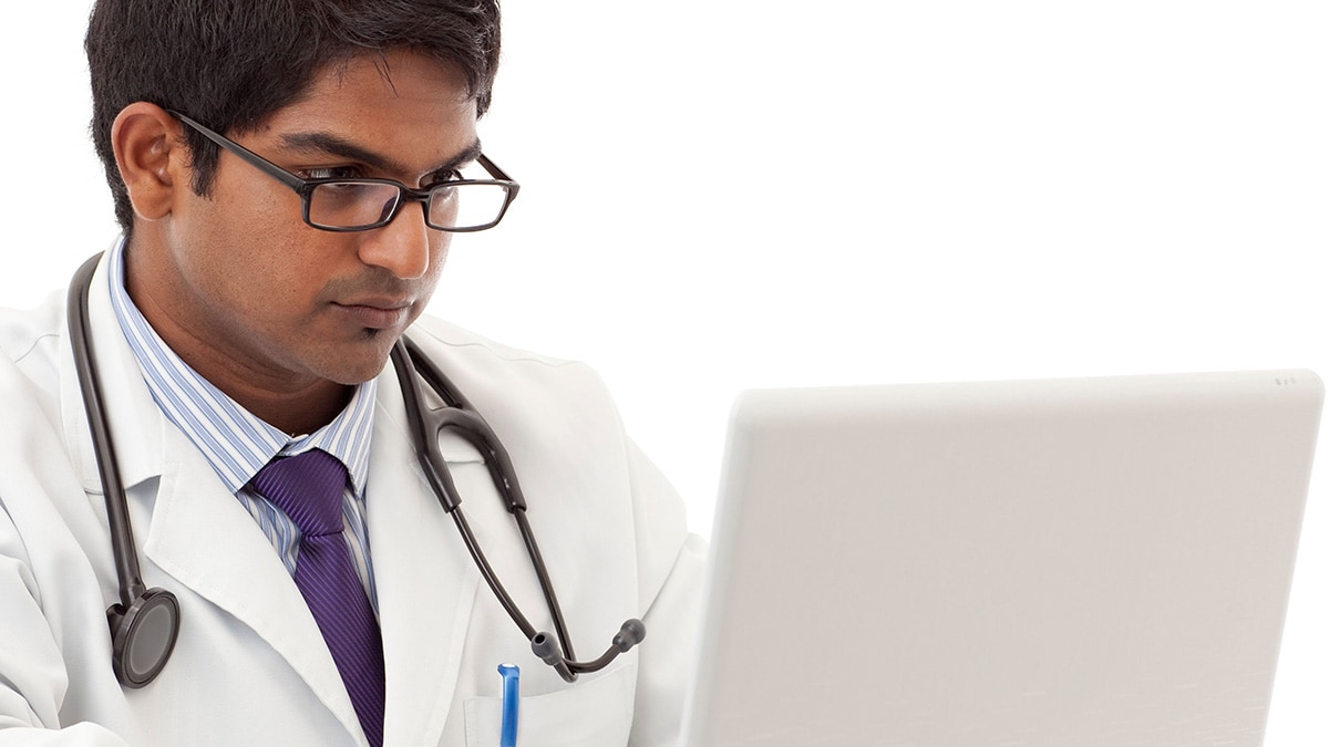 Male healthcare provider with serious face working on laptop