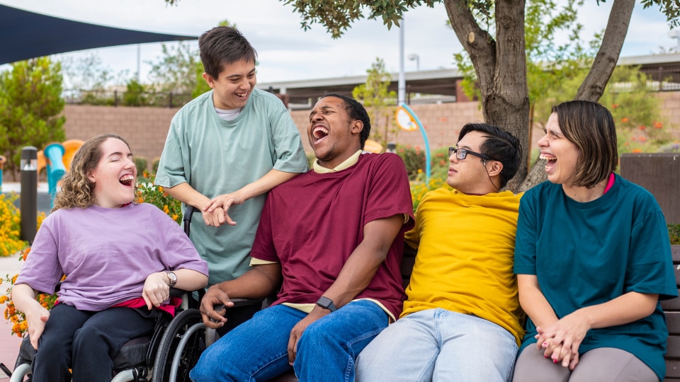 Group of young adults with various physical disabilities laughing together.
