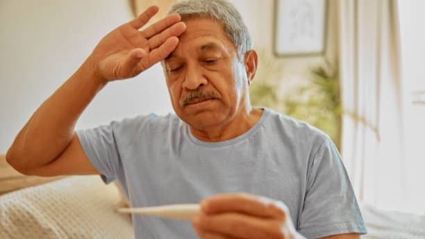 Older man looking at thermometer with hand on his forehead