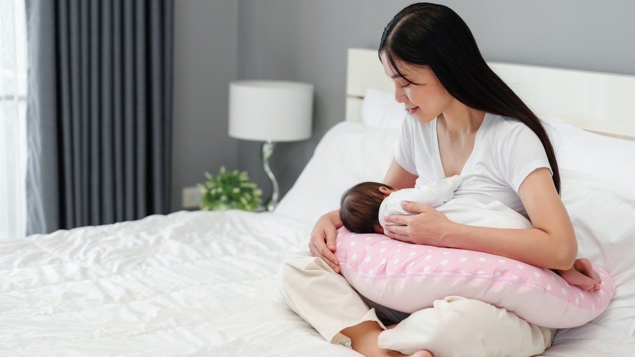 Mom sits on a bed and breastfeeds her baby.