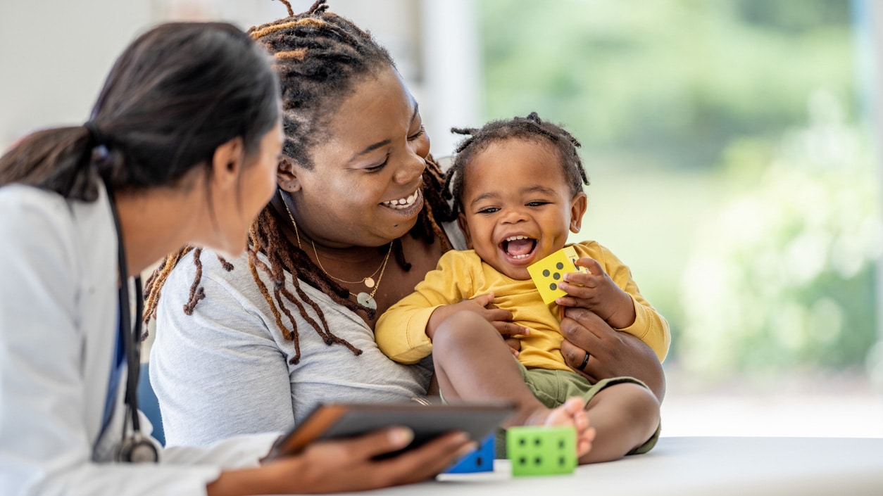 A mom holding her toddler with a health care professional looking on.