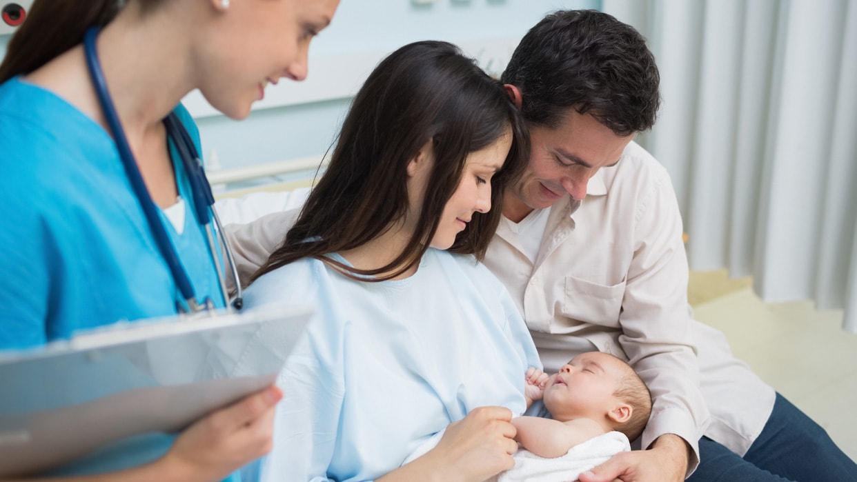 Doctor looks at a mom and dad holding a baby in diaper in a hospital room.