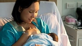 Woman breastfeeding an infant in a hospital room.