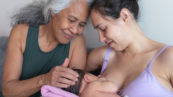 A woman breastfeeding a child while a grandmother offers support.