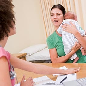 Health care provider talking with a woman holding an infant.