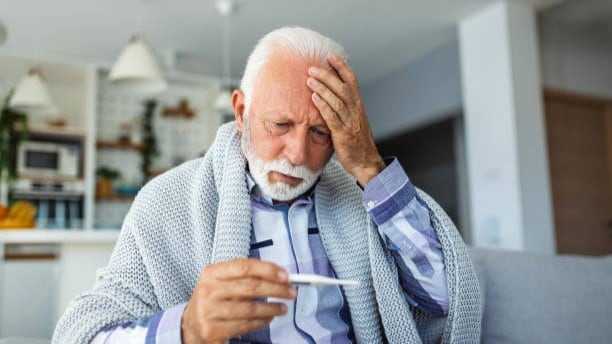 Older man looking at thermometer with hand on forehead