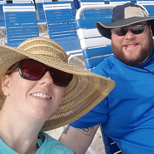 MaryBeth and Brandon wearing wide-brimmed hats and rash guards at the beach.