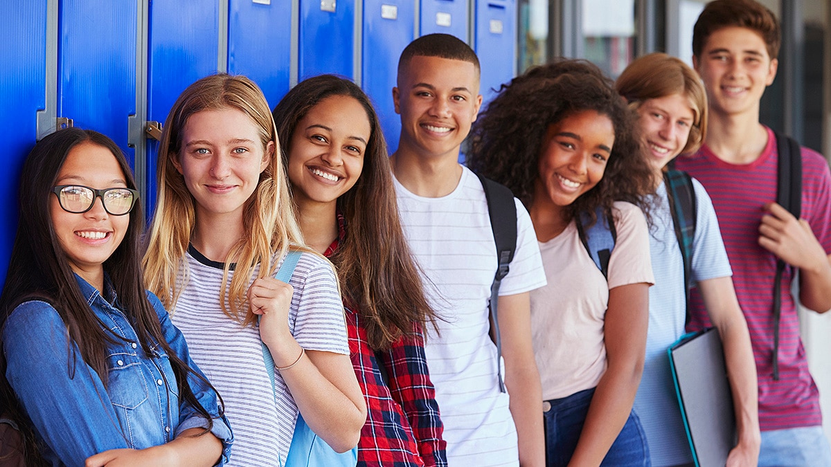 High school students standing in a row in front of blue lockers.