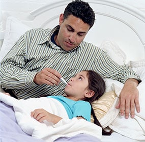 Father taking temperature of sick daughter in bed.