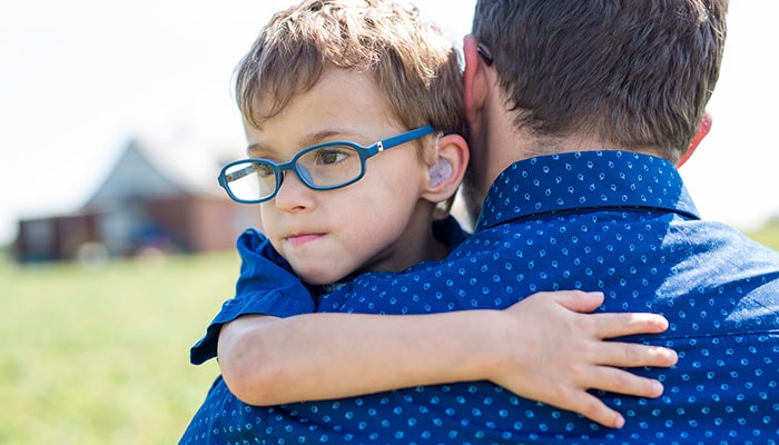 Un niño con un audífono abrazando a su padre