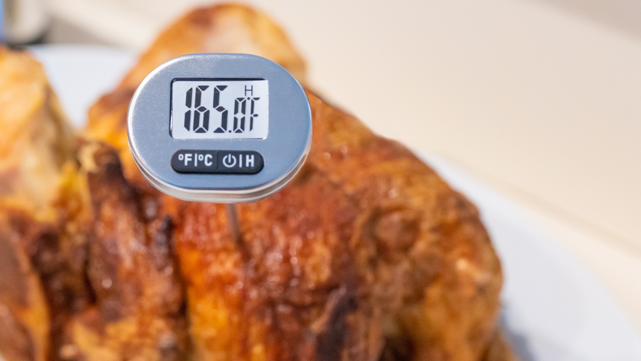 Rotisserie chicken with food thermometer showing the chicken has been cooked to a safe internal temperature of 165 degrees Fahrenheit.