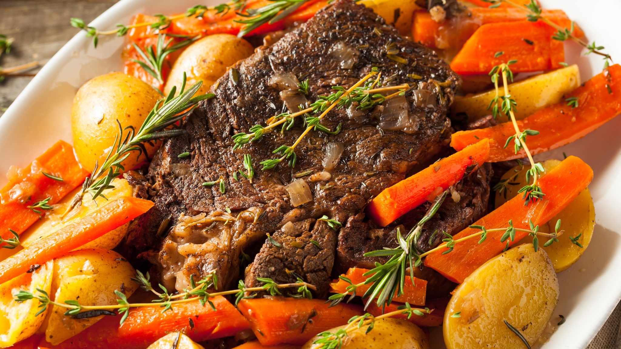 A dish of cooked roast beef, carrots, and potatoes.