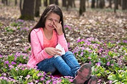 Una niña con picazón en los ojos sentanda entre flores.