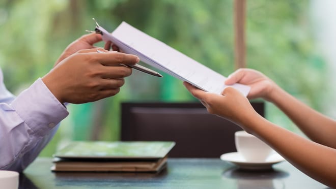 A worker hands a contract to a co-worker.