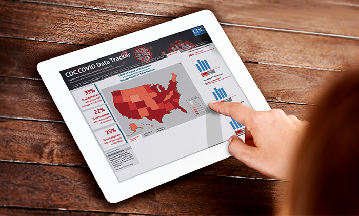 Looking over shoulder as a finger taps the screen of a digital tablet.