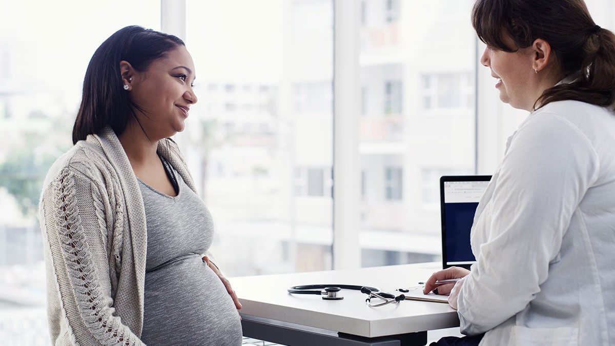 Young pregnant woman discussing the benefits of vaccination with her OB/GYN.