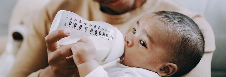Baby boy being bottle-fed milk at home by his father