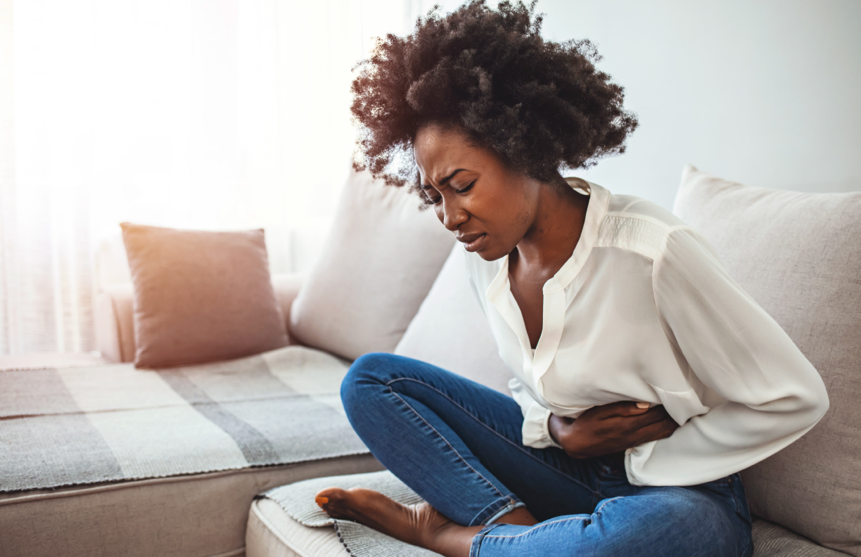 Mujer sentada en el sofá agarrándose el estómago de dolor.
