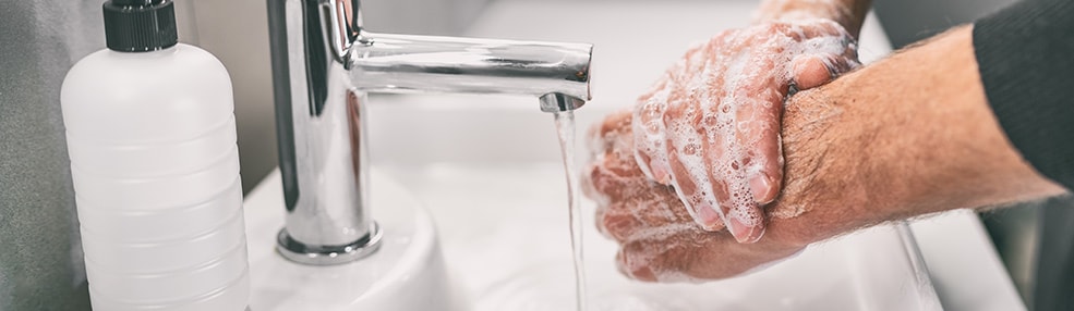Close up of man's hands at a sink with soap on them and water running.