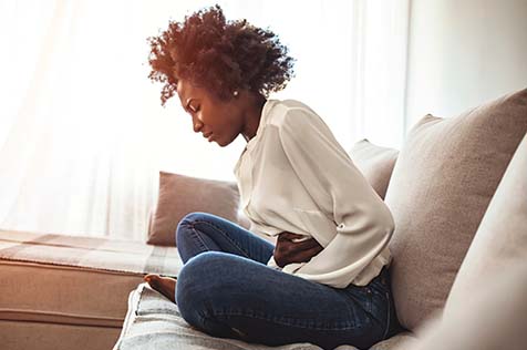 Woman sitting on the couch holding her stomach in pain