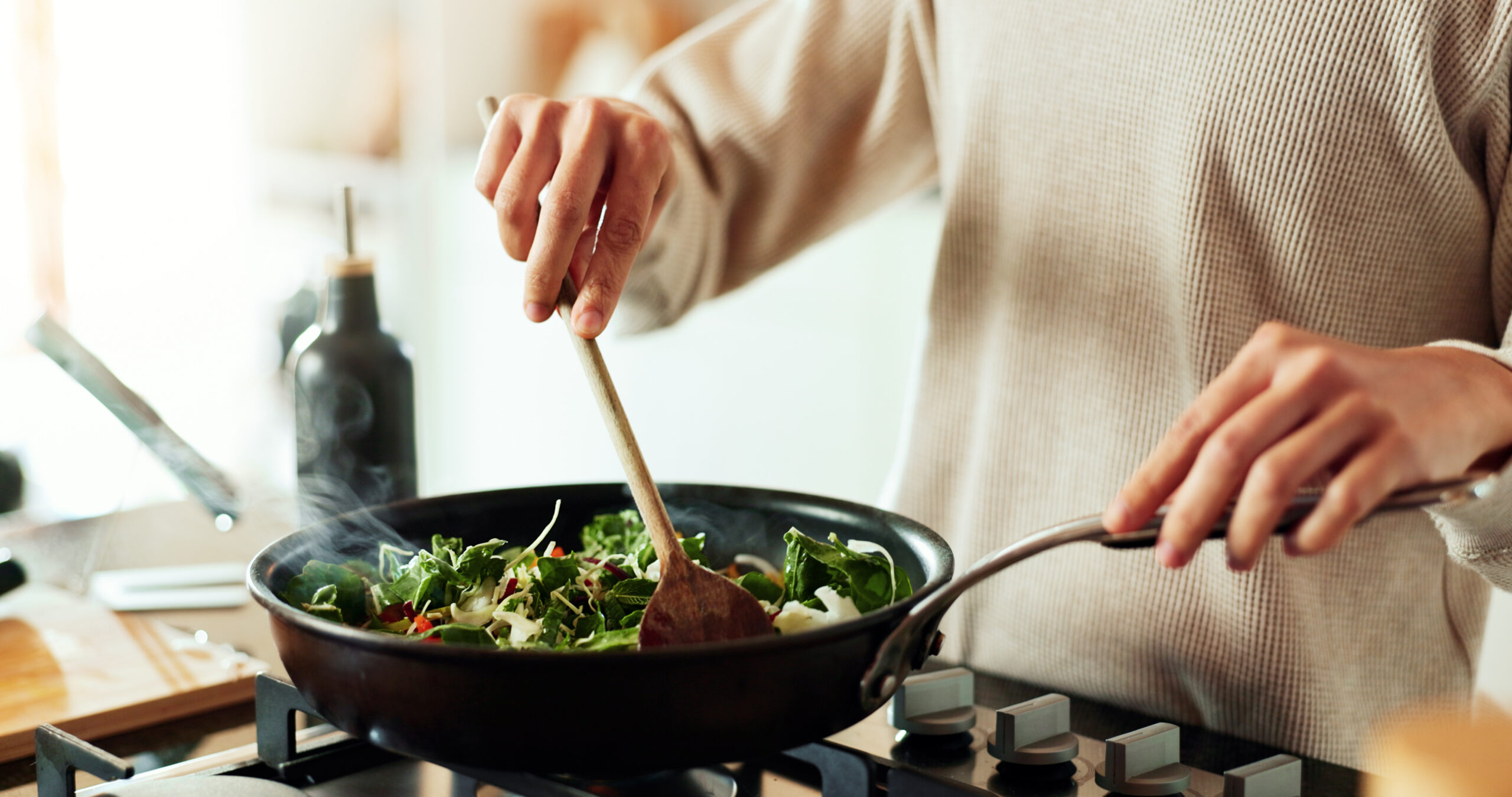 A woman stirs a pan of vegetables cooking on a stovetop.