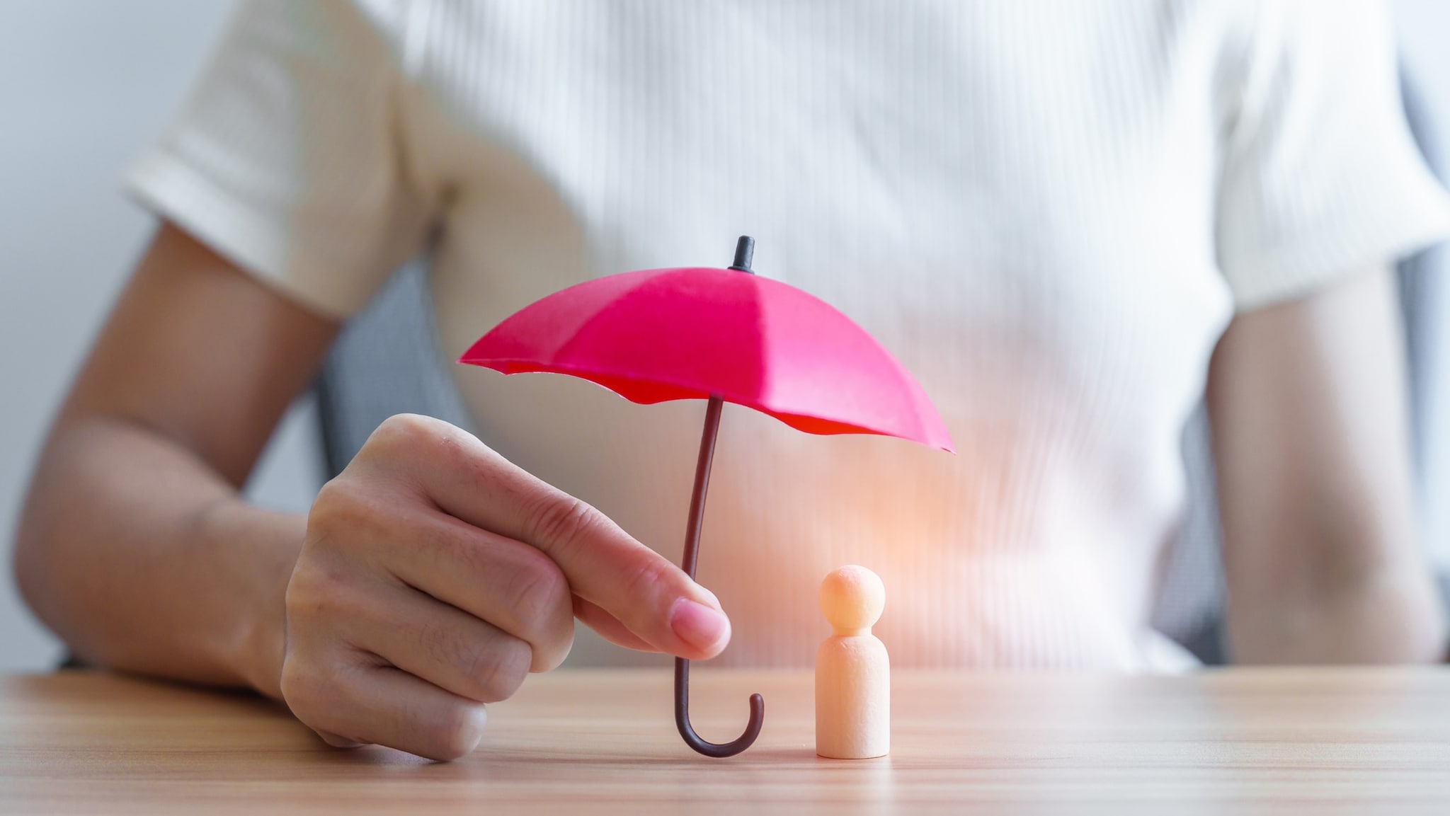 A person holding a miniature umbrella over a wooden person figure