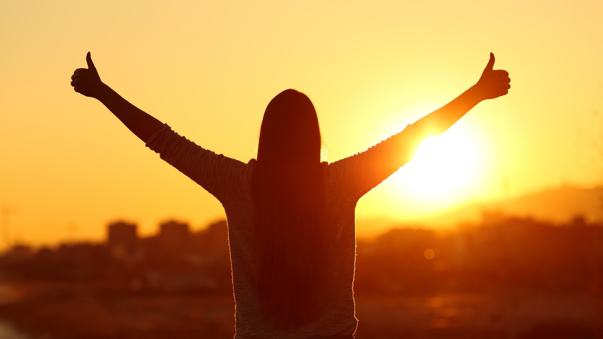 Woman standing and facing the sun with two thumbs up